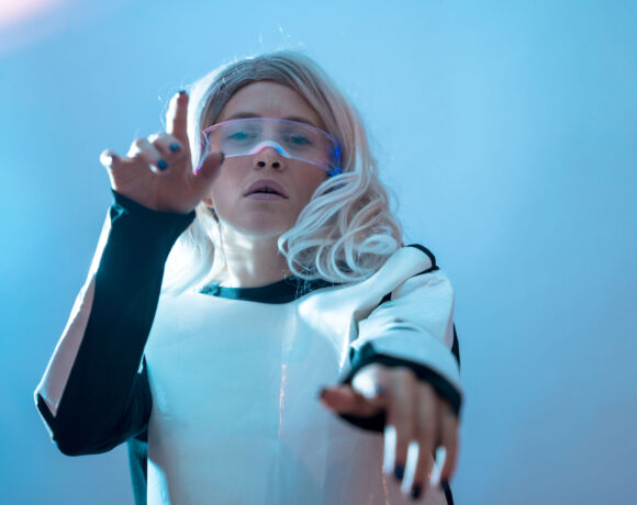 Woman watching with the illuminated futuristic glasses, blue background, moving the controllers in virtual reality